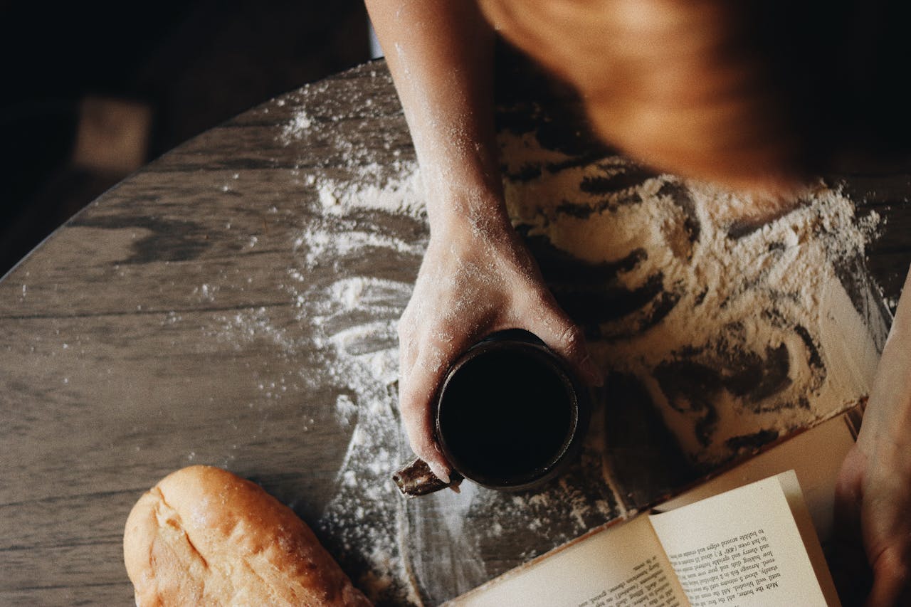 Woman preparing dough with coffee and recipe book, creating a warm home baking atmosphere.